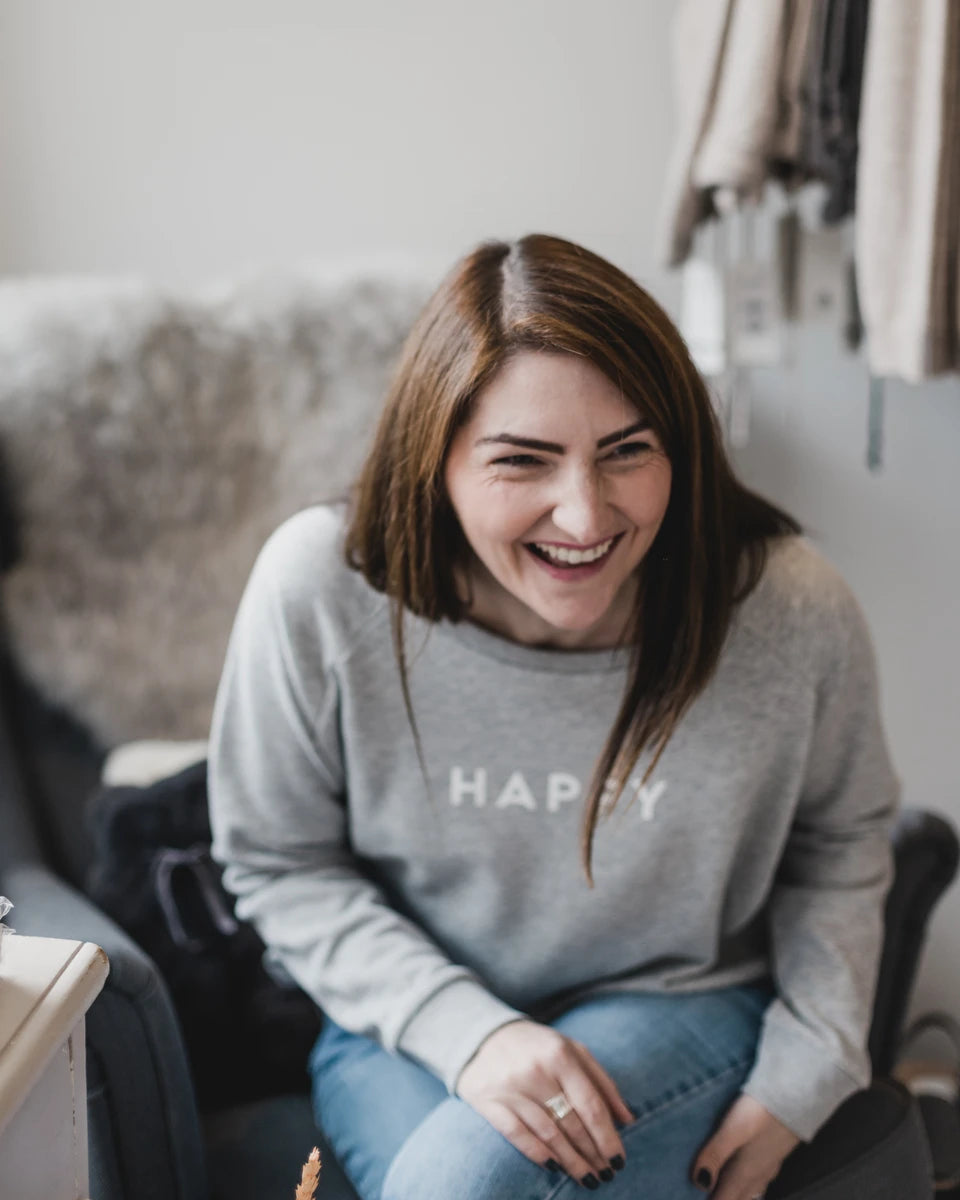 Suzie, owner of SELF, sat on a dark grey chair laughing