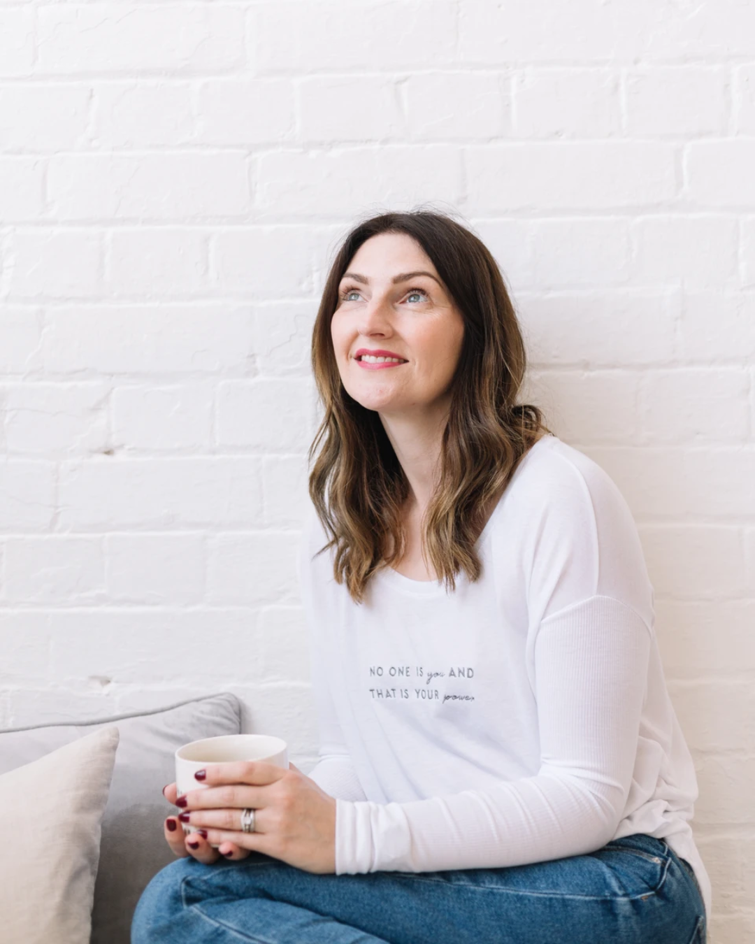 Suzie, owner of SELF, sat with a cup of tea next to some plush cushions, looking upwards