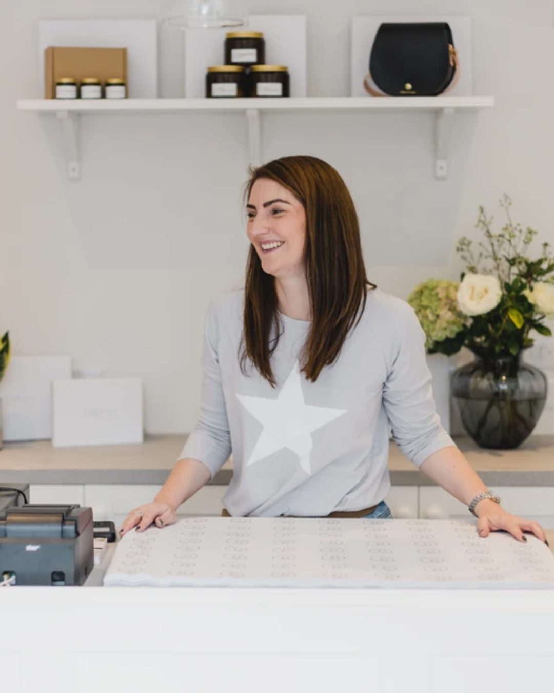 Suzie, owner of SELF, sat on bench seating with a cup of coffee in hand smiling towards the camera, holding a lifestyle magazine